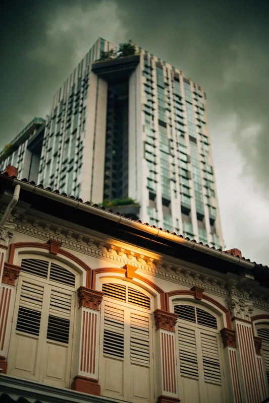 Batu & Beam — restored Peranakan shophouse facade against a blurred modern tower under a monsoon sky